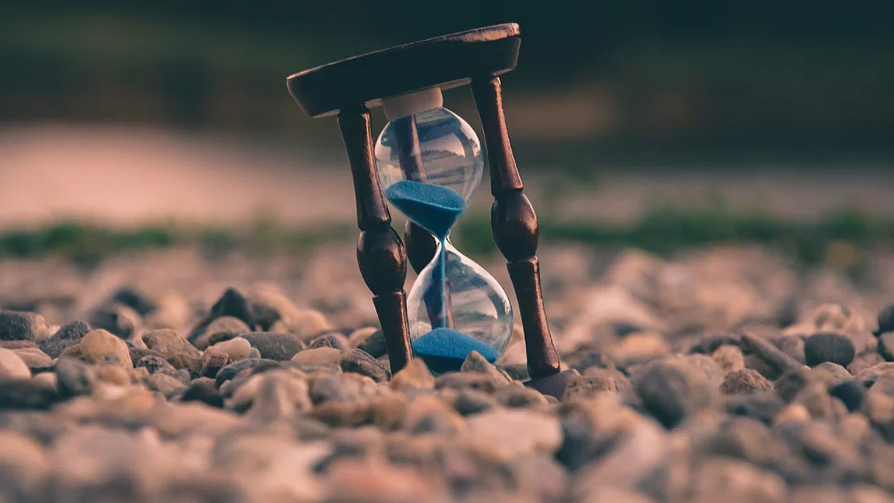 An hourglass standing on stones with the sand part way through
